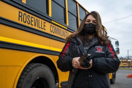 Roseville electric school bus with driver (Jennifer Lewis) holding charger