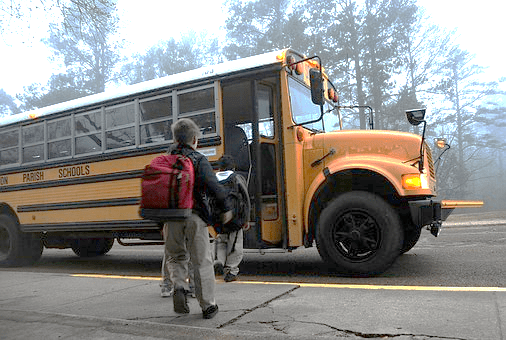Schoolchildren waiting to board a yellow school bus.