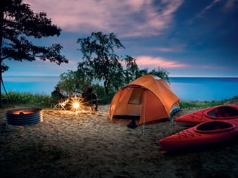 people sitting in chairs on beach with tent, kayaks, lake in background