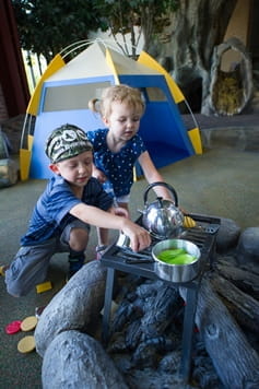 boy and girl pretending to cook over campfire at the Outdoor Adventure Center campsite exhibit boy and girl pretending to cook over campfire at the Outdoor Adventure Center campsite exhibit