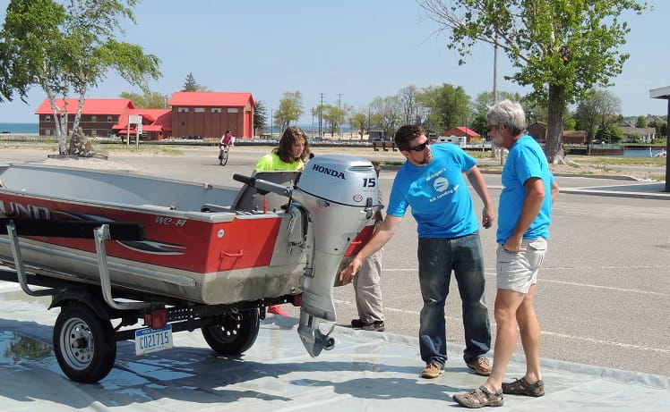 Two volunteers show a boater where to remove debris from a trailered fishing boat.