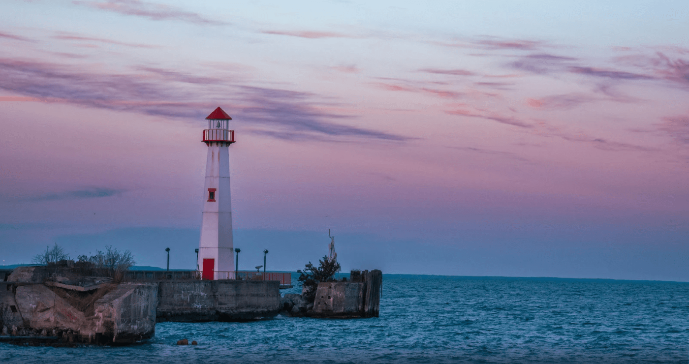 lighthouse at waters edge with a colorful sunset in background