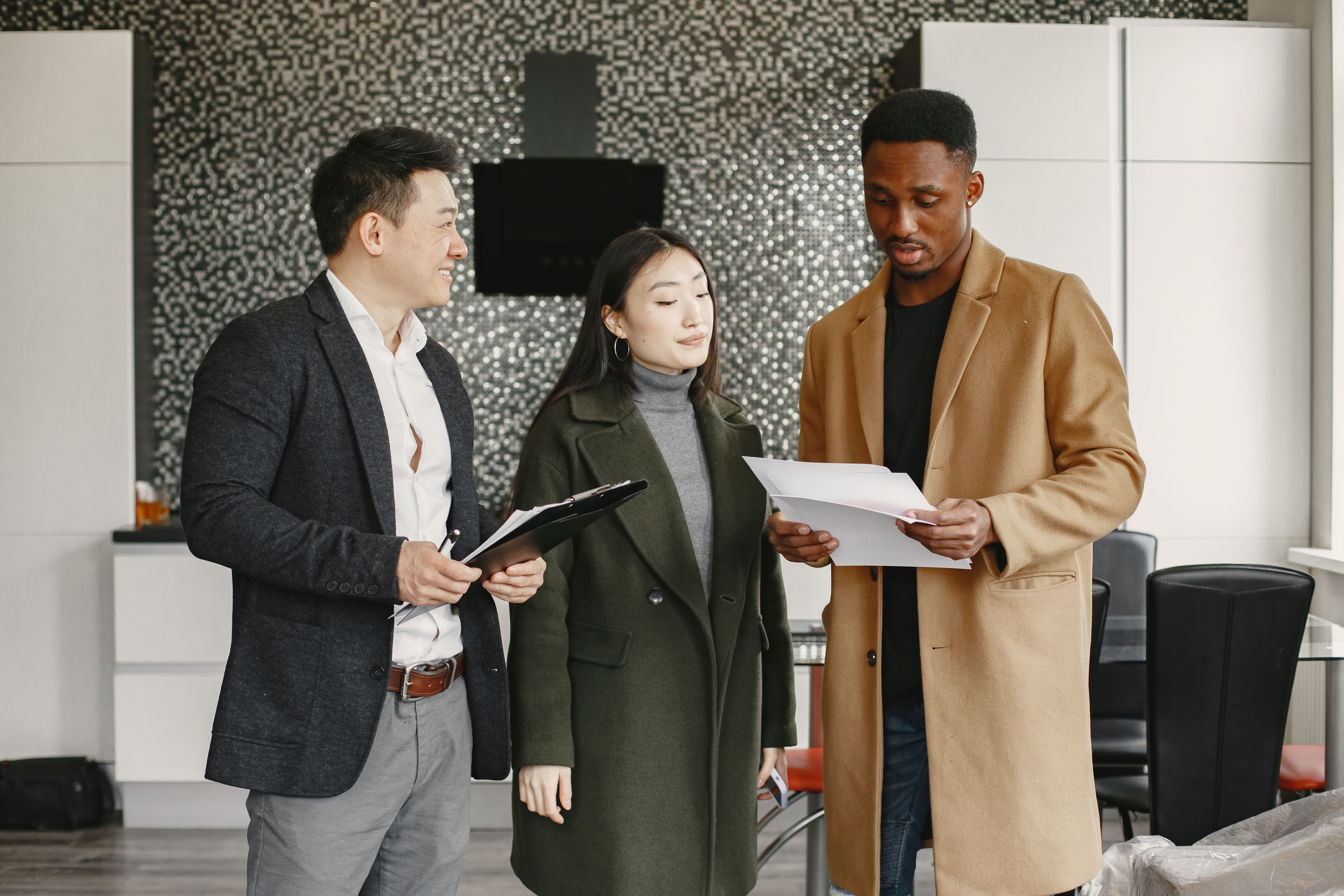 Asian man, Asian woman and Black man in business attire review documents in an office setting