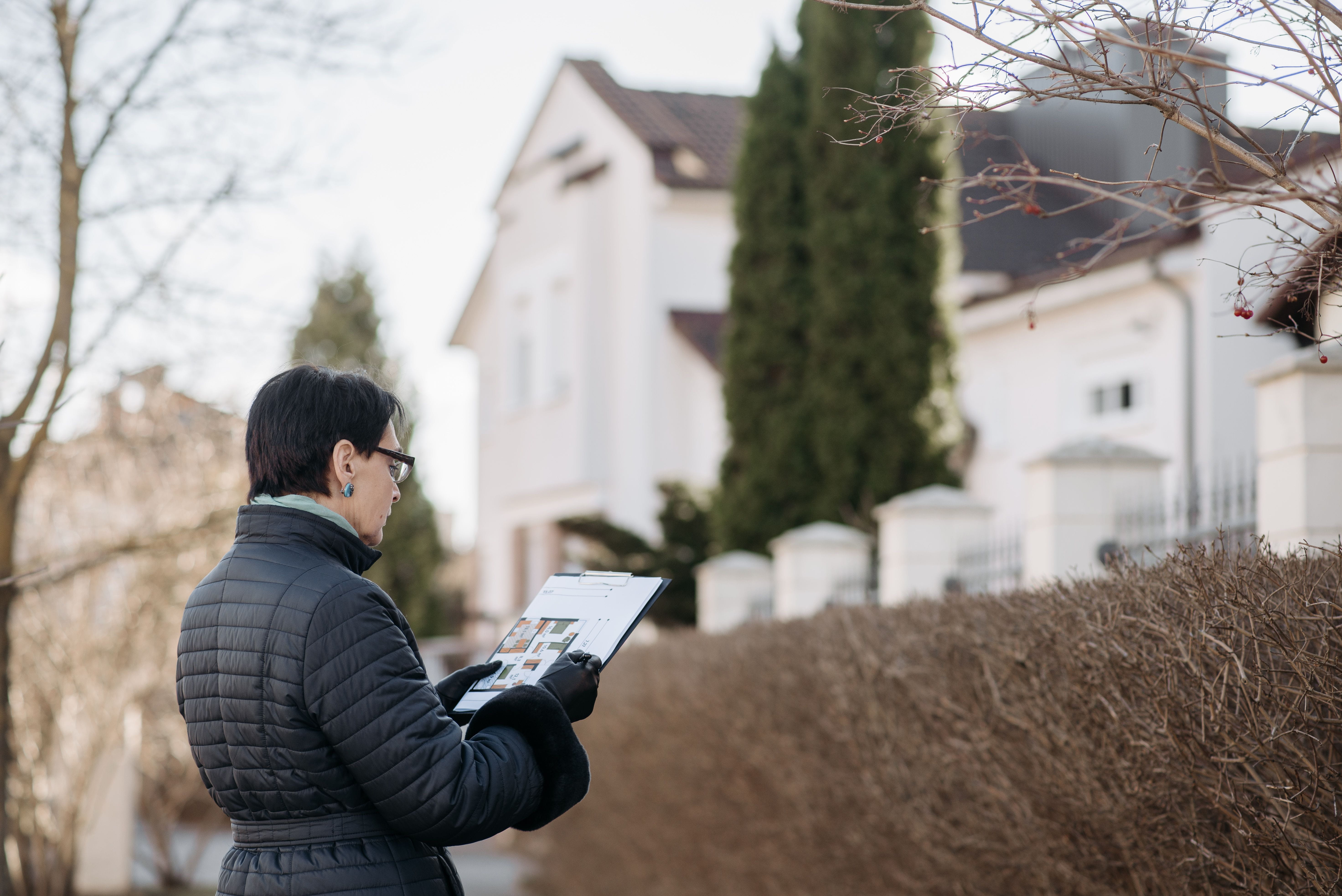 Real Estate Appraiser evaluates the outside of a home while reviewing floorplans