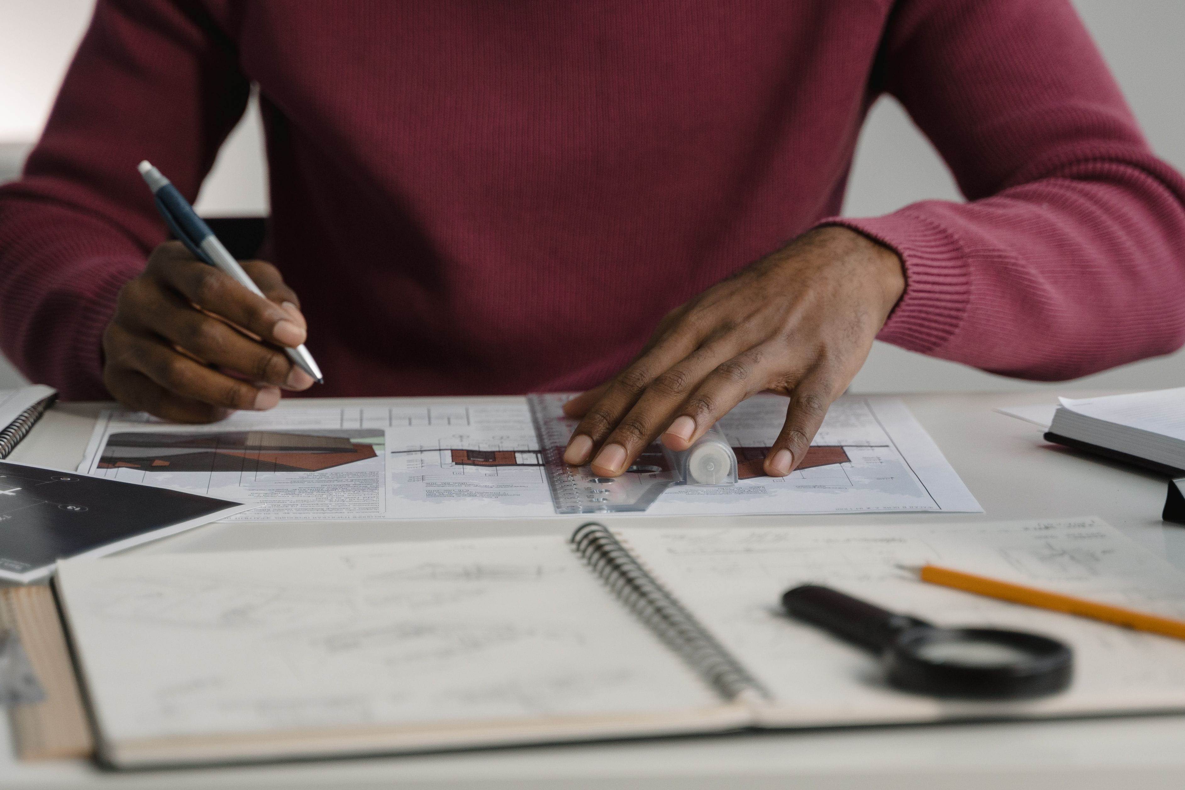Architect holding a pencil sitting at a table with notebooks and blueprints