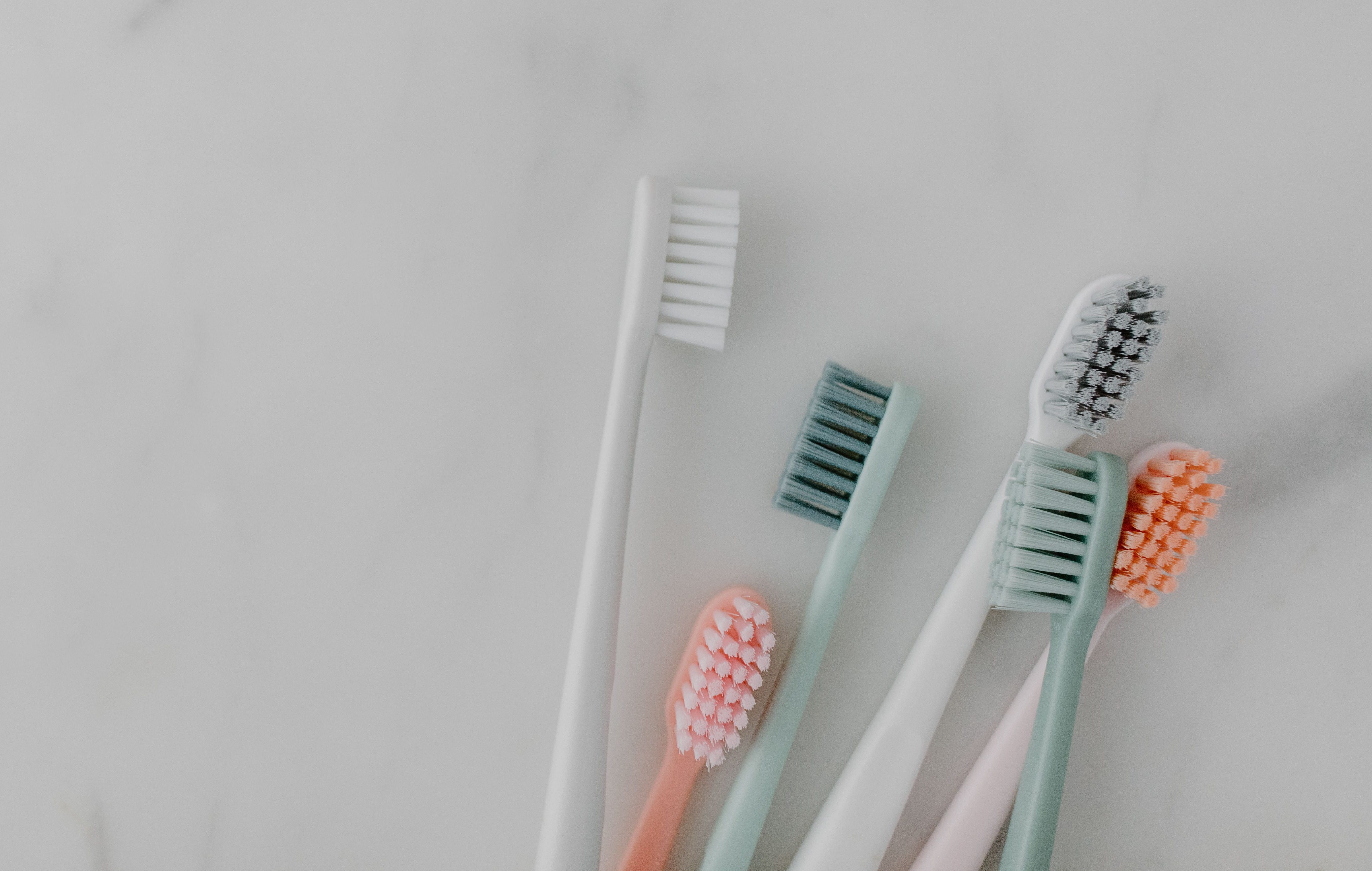 Six multi colored toothbrushes on a off white background