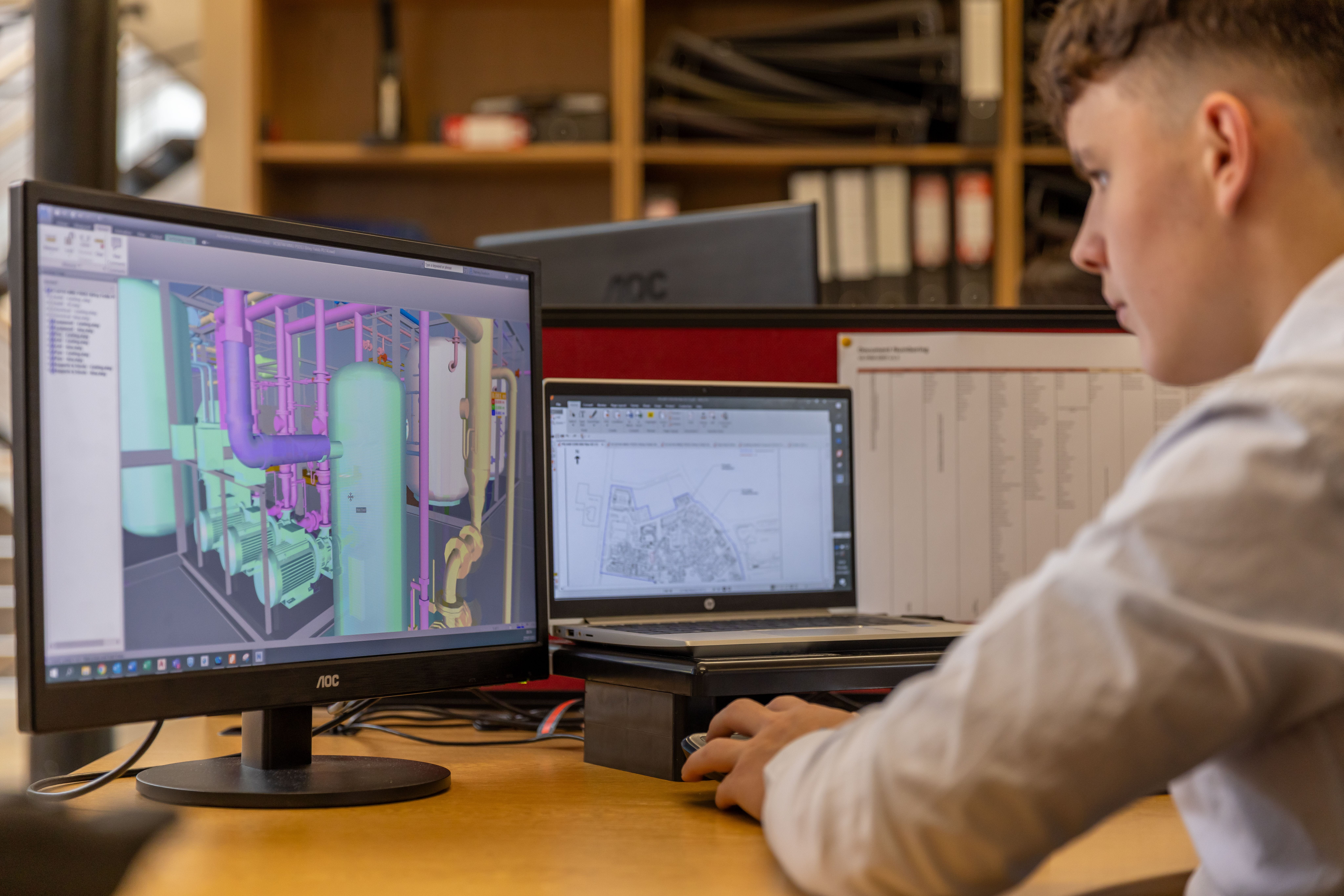 Man at desk with laptop and monitor using CAD software