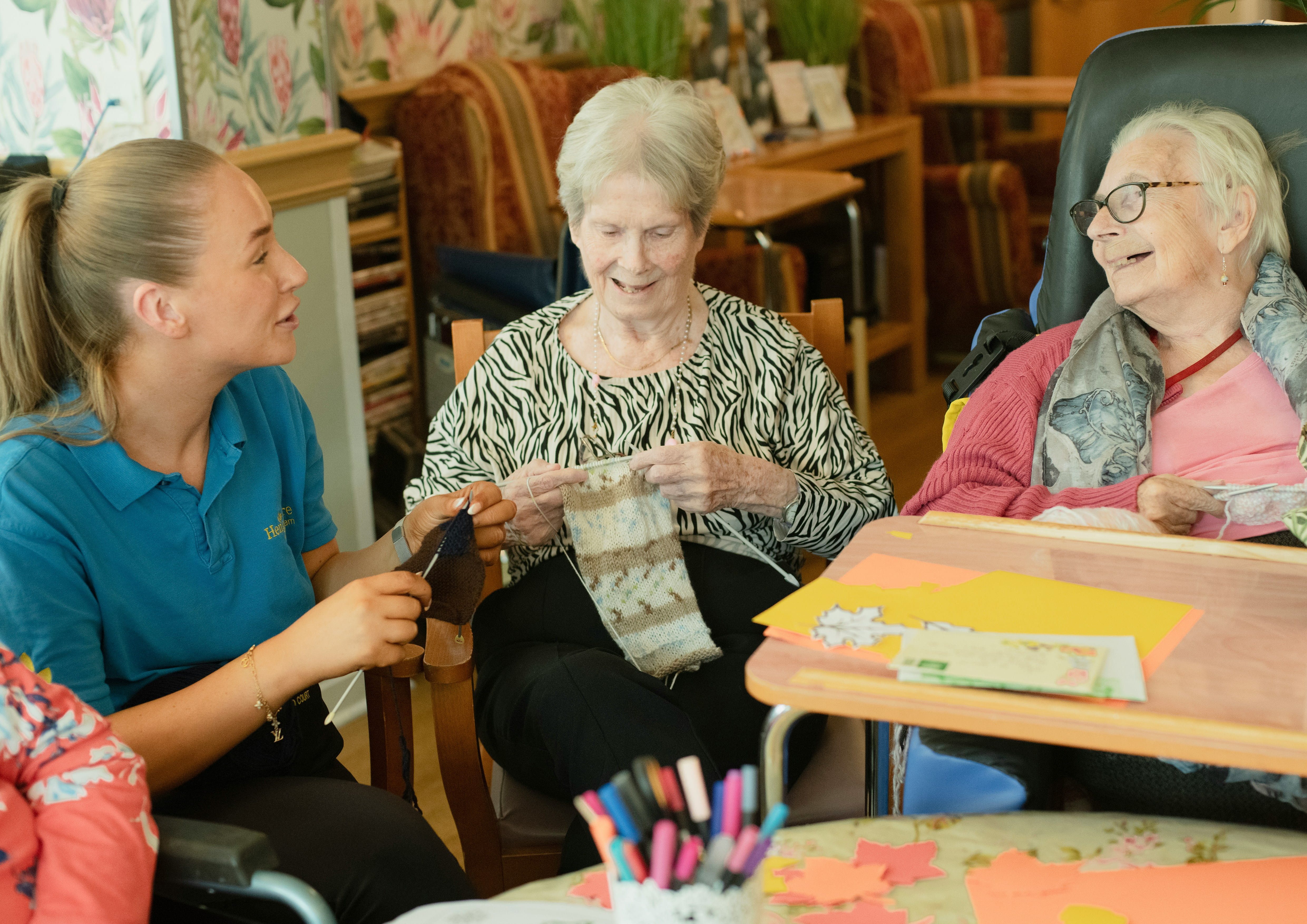 Two elderly women crochet with a nursing home employee