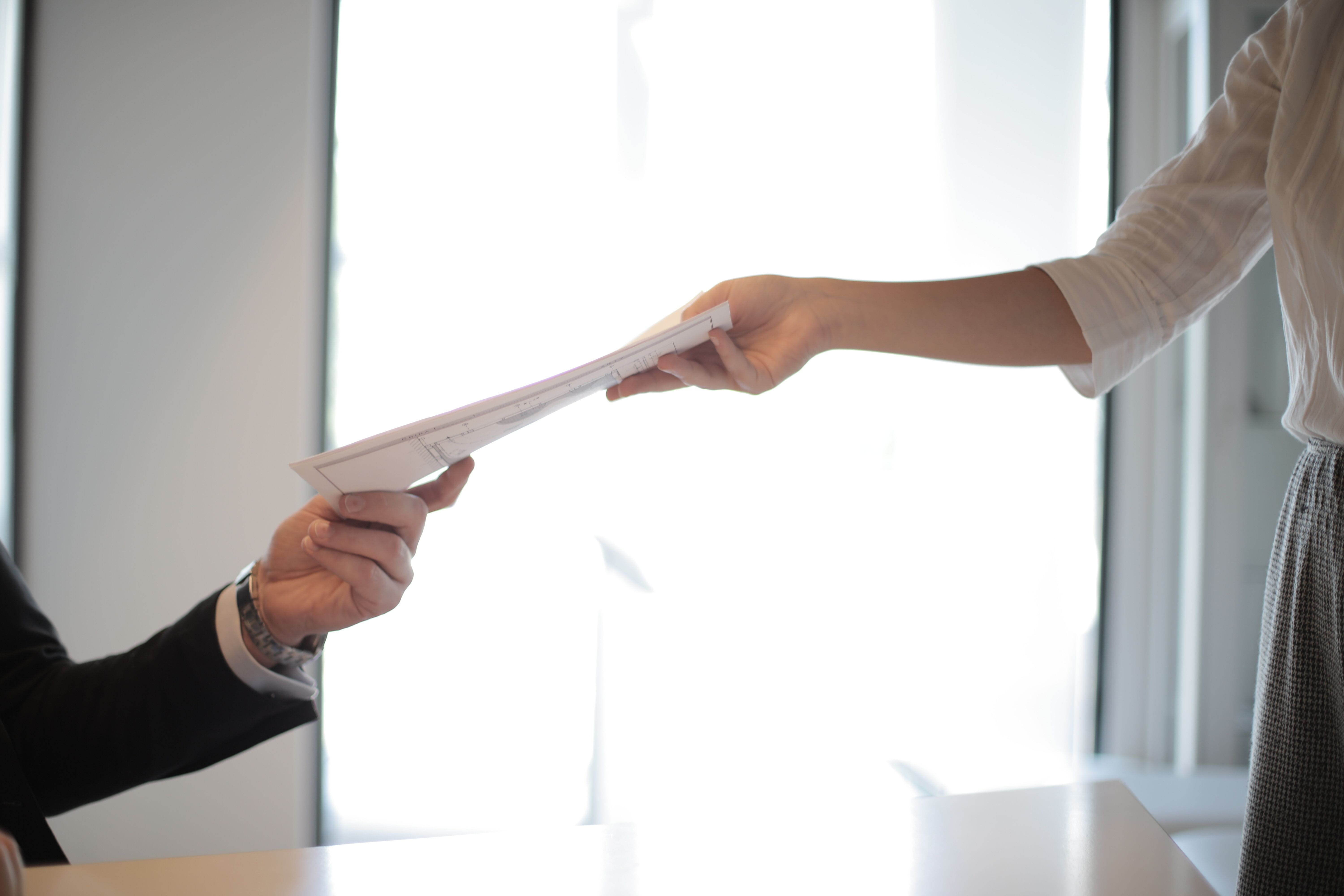 Man in suit giving resume to woman in business attire standing across the table from him