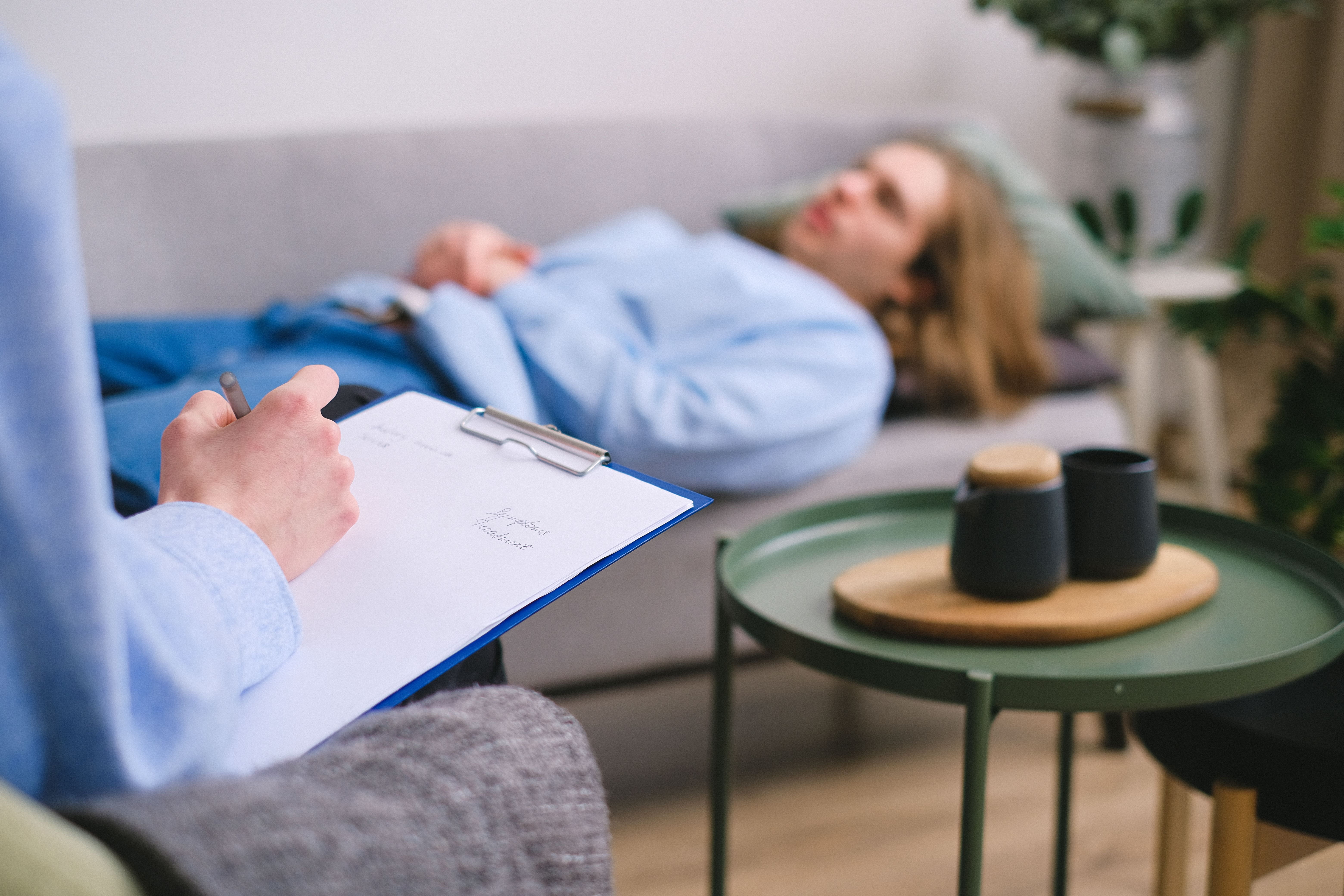 Psychologist with clipboard across from patient lying on sofa