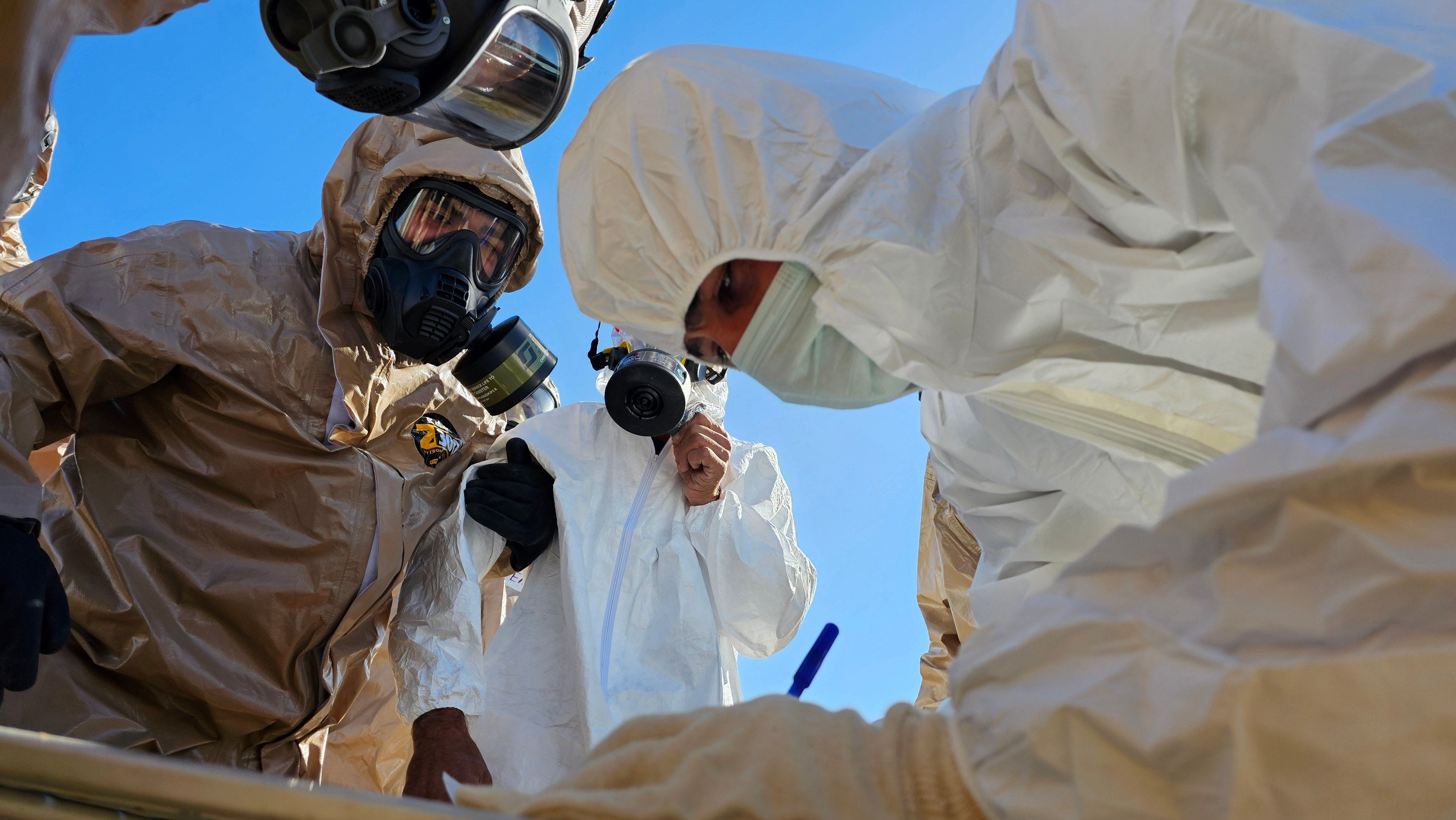 Sanitarians in hazmat suits watching as one of them takes notes