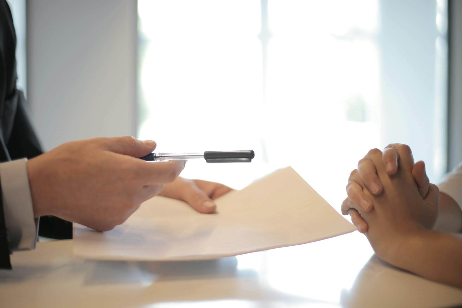 Person handing another person forms and a pen.