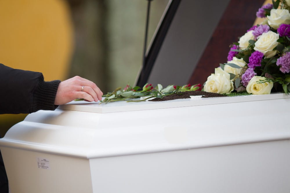 A persons had on a white casket topped with white and purple flowers