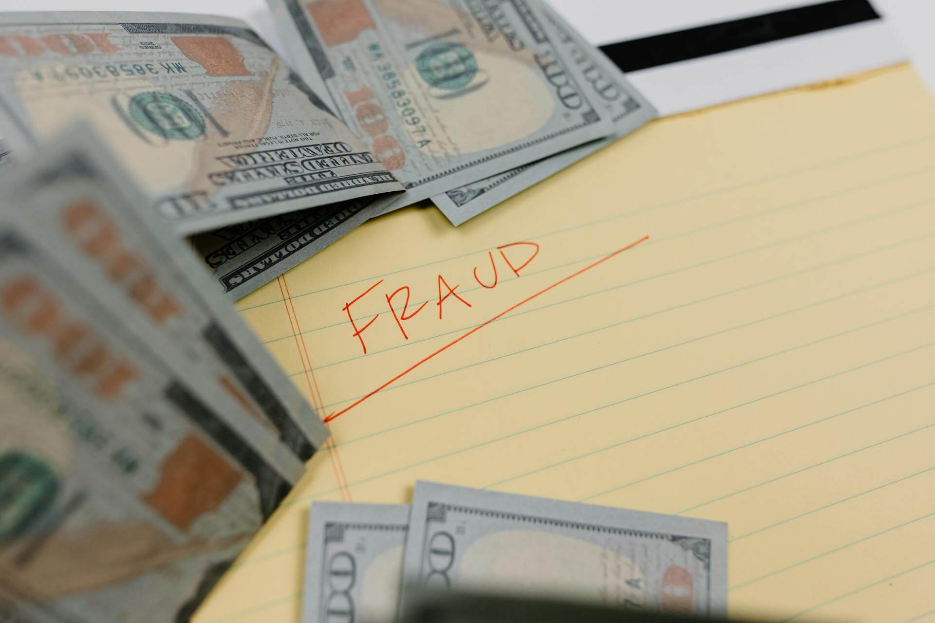 100 hundred dollar bills on a yellow notepad with "Fraud" written on it