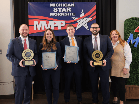 Five individuals stand together holding awards at the MIOSHA MVPP Star award ceremony, posing in front of a 'Michigan Star Worksite MVPP' banner.