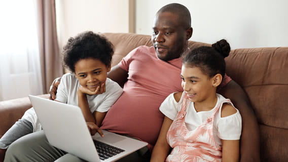 father on couch with young daughter and son looking at computer