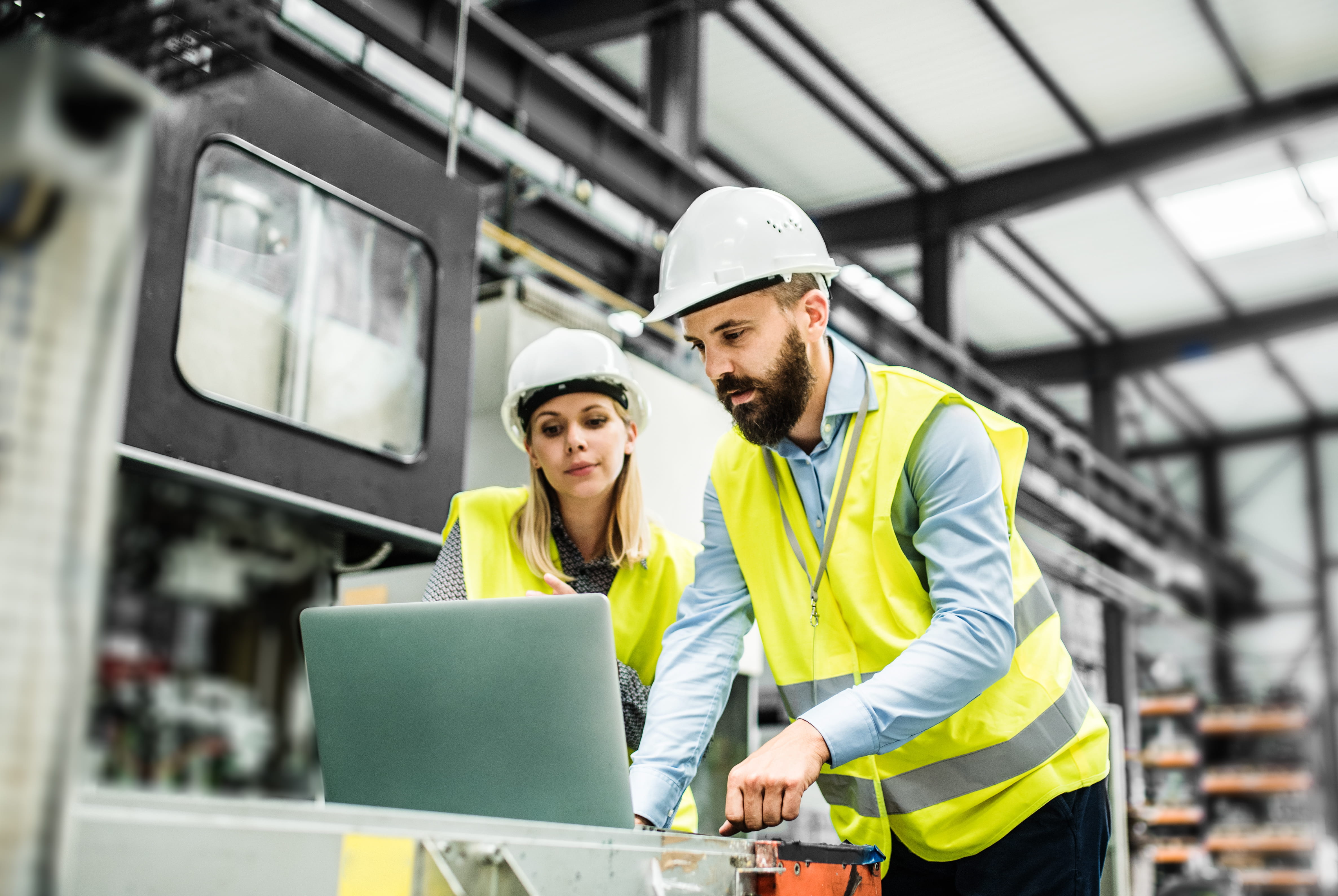 Two people in hard hats looking at a laptop.