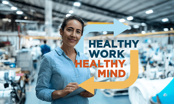 Woman smiling while holding a clipboard in a factory with Healthy Work Healthy Mind overlayed