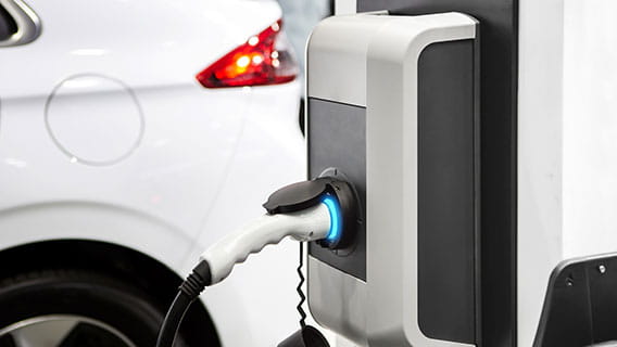 A white electronic vehicle plugged into a charging station