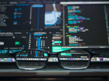 Glasses on desk-computer screen data in background