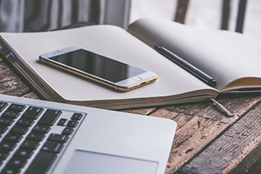 Laptop, open notebook with pen, phone 