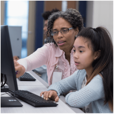 A teacher helping her student on a computer. 