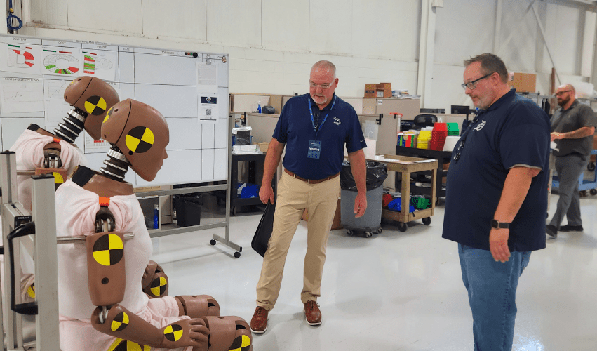 (Left to right) MIOSHA Director Bart Pickelman observes a crash test dummy with Humanetics QMS Facilitator Josh Yingling during a MIOSHA Take a Stand Day consultative visit.