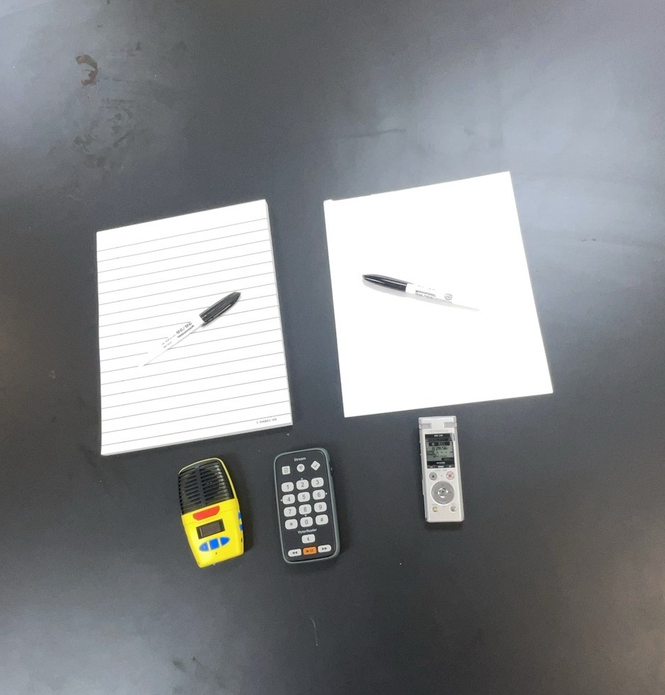Notetaking tools including white paper pad with black markers; small recorder; Braille notetaker