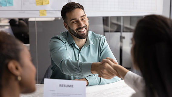 a male interviewee shaking hands with female interviewer while another female interviewer holds his resume