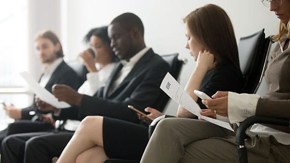 row of waiting potential employees in business clothes sitting against a wall reviewing notes and resumes