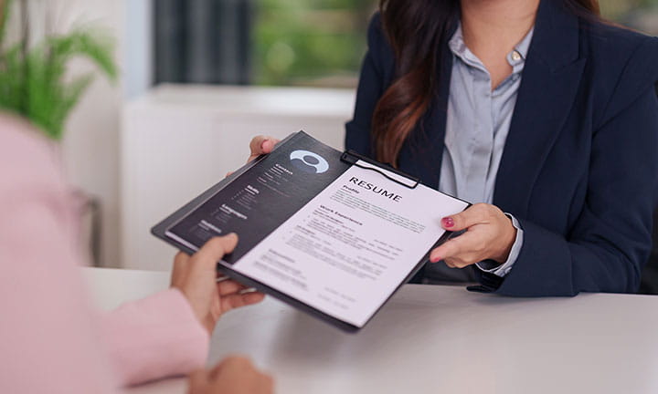 a woman in business clothes sitting at a table handing her resume off to another woman in business clothes