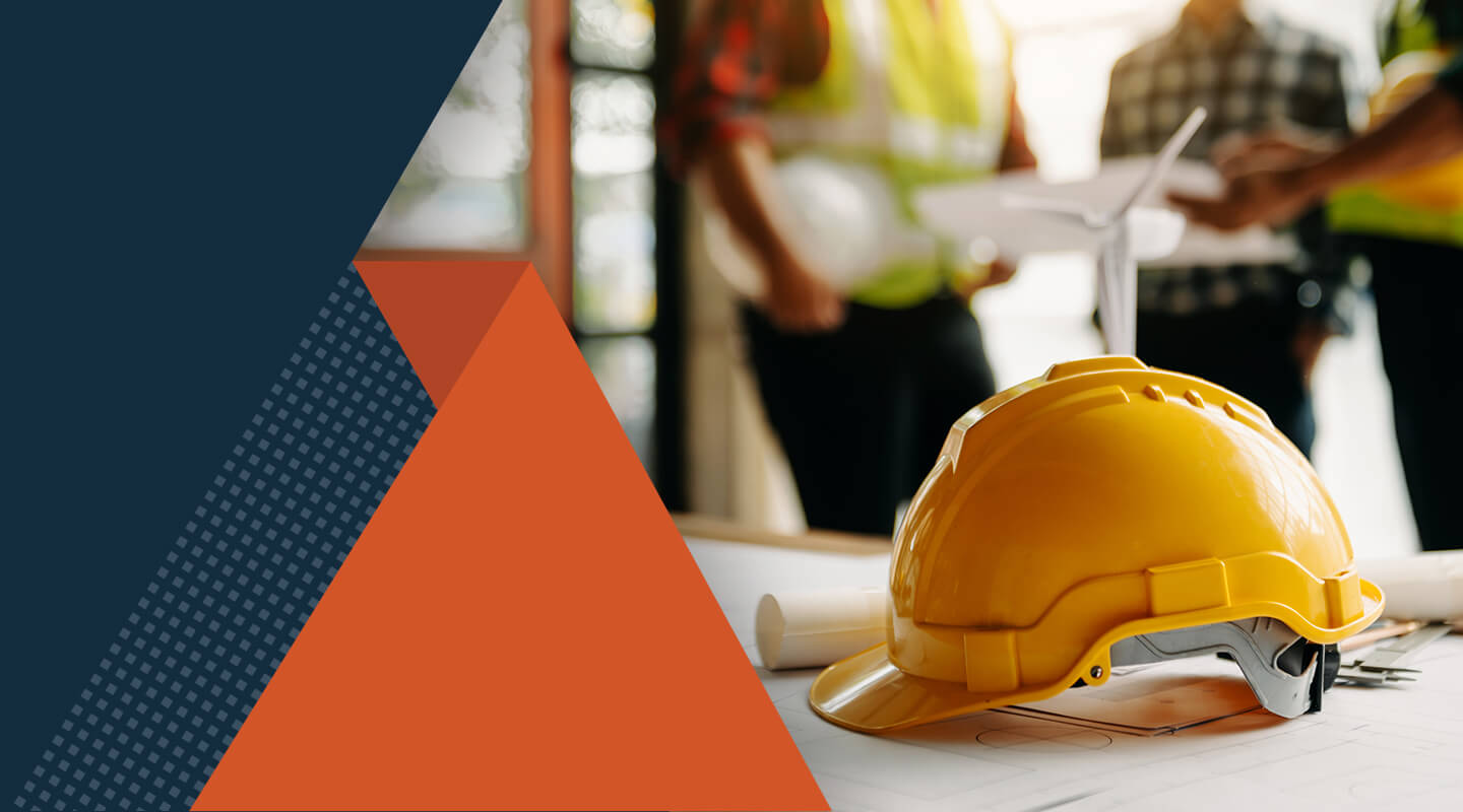 A yellow construction hard hat rests on architectural blueprints on a table, with rolled papers nearby and a small group of people in safety vests standing and discussing plans in the background. Geometric shapes in dark blue and orange overlay part of the image.