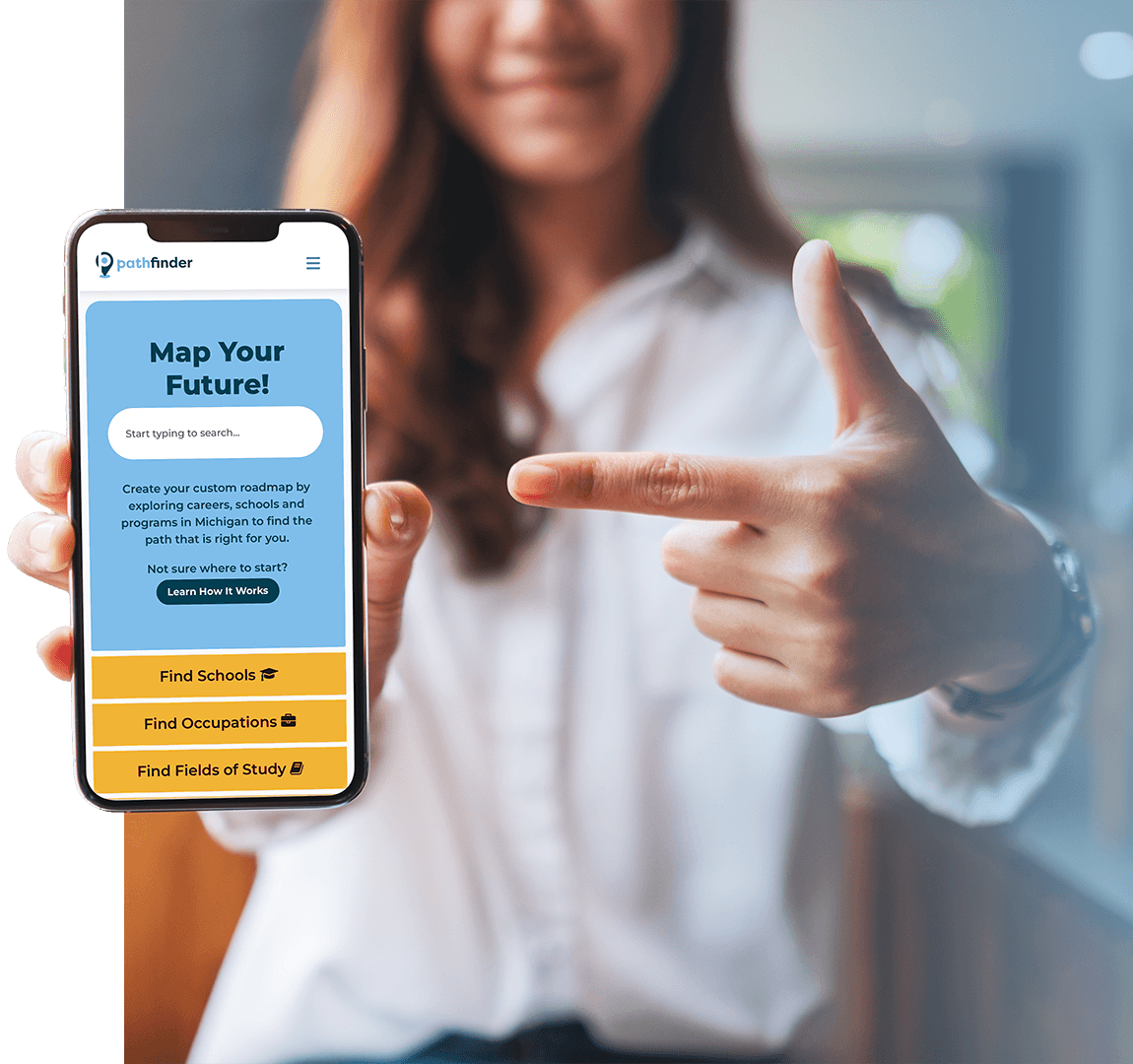 Person holding a smartphone displaying the Michigan Career Pathfinder website interface with options to search for schools, occupations, and fields of study. The other hand is pointing toward the phone. The background shows an indoor setting with soft lighting.