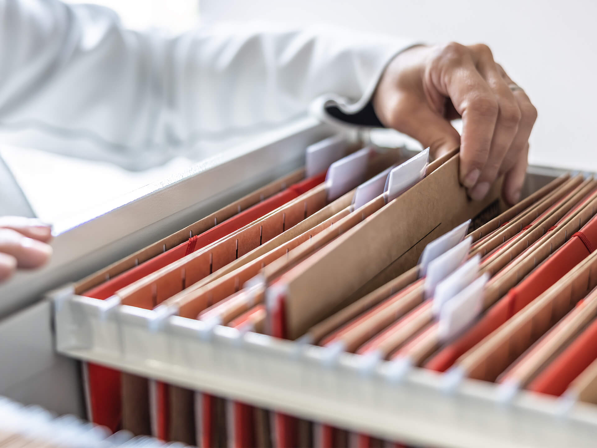 Close-up of a hand retrieving a file folder from a filing cabinet, with organized rows of folders containing documents.