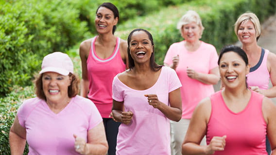Diverse group of six women wearing pink and smiling, running in a breast cancer run