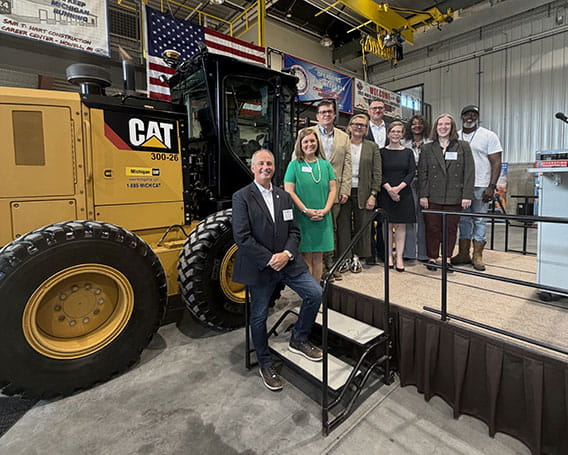 nine people pose on a platform next to a tractor to commemorate the signing