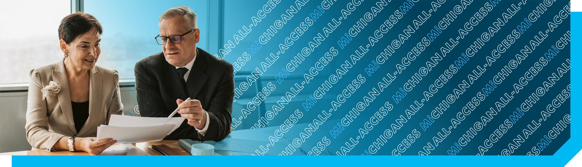 Two business professionals dressed in boardroom attire sitting together at an office conference room table reviewing documents.