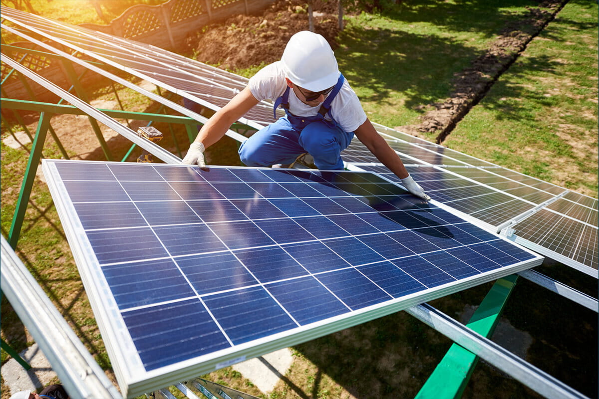 An energy worker crouching down to install a solar panel on a sunny day.