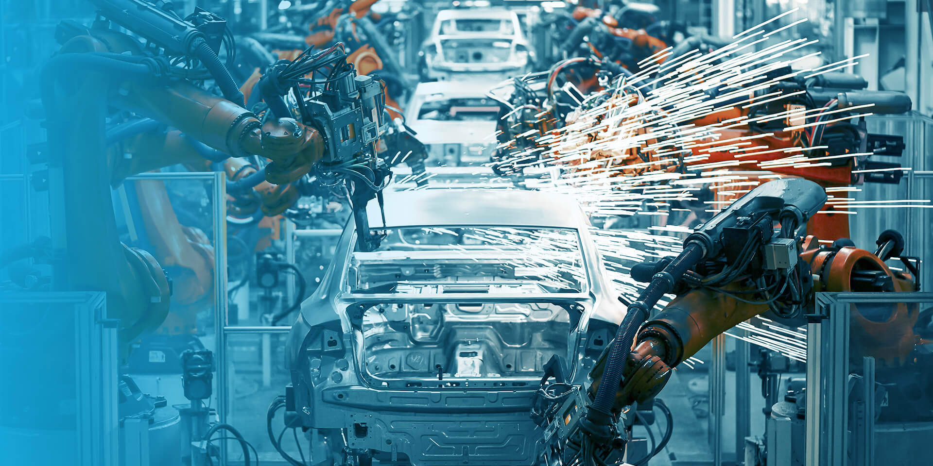 Industrial robots welding the frame of a car on an automotive assembly line, with bright sparks flying around the vehicle body.