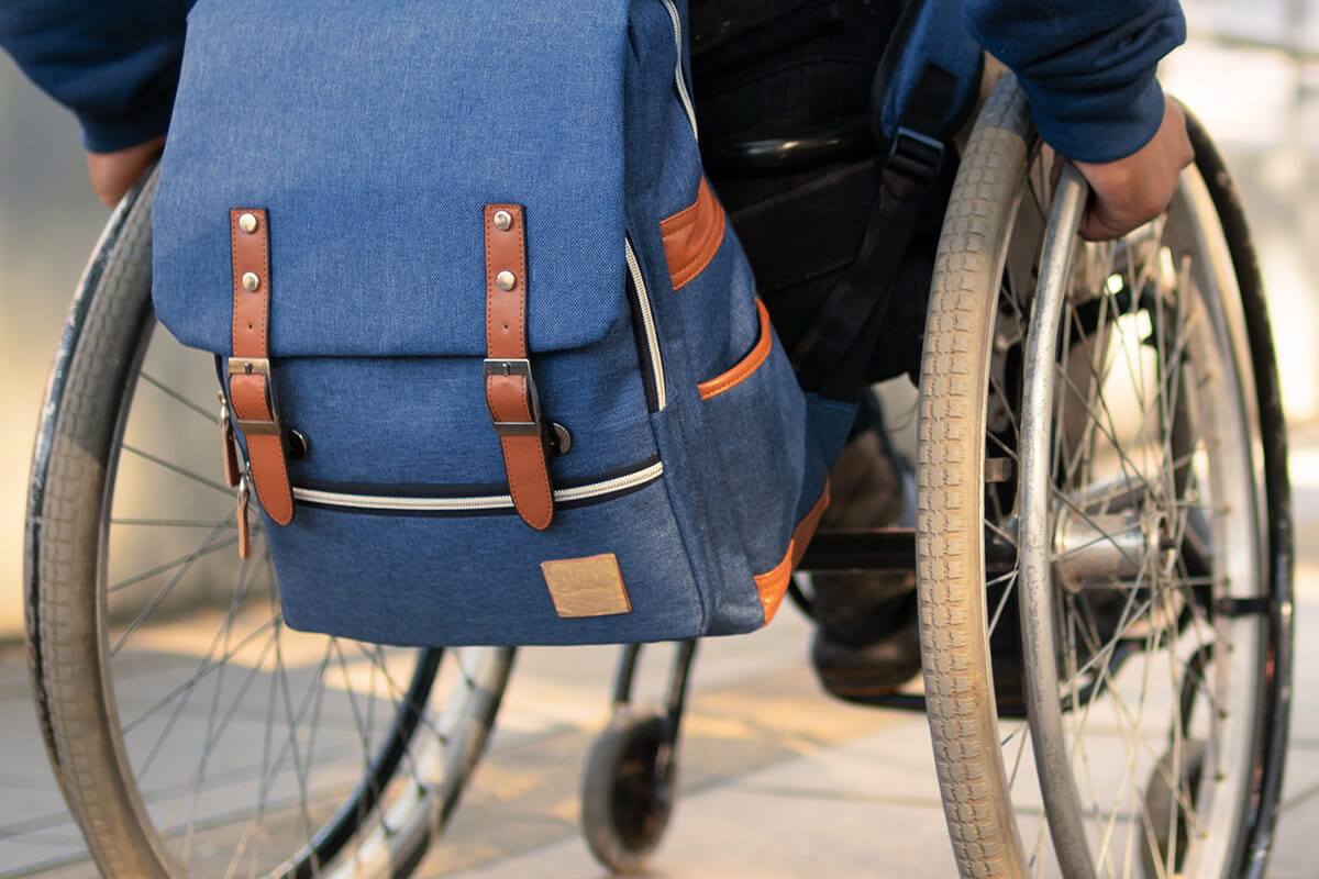 Closeup of a wheelchair with a backpack strapped to the back.