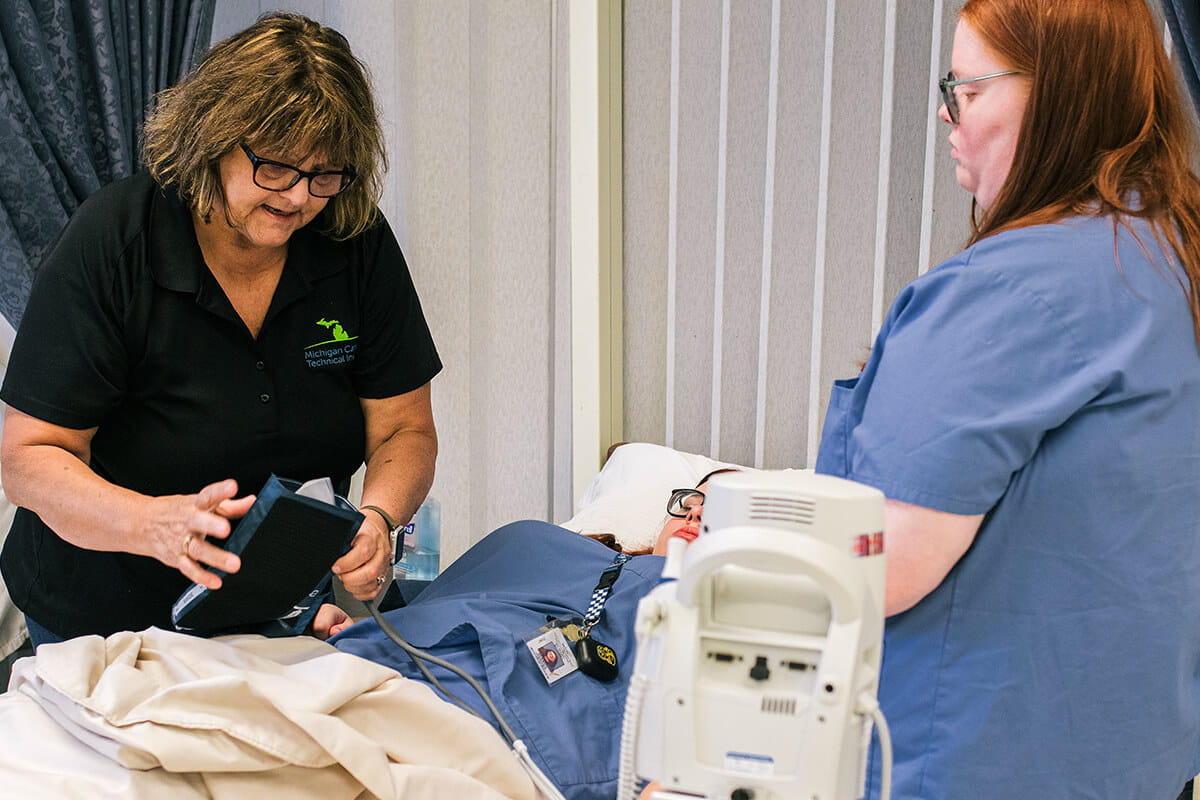 MCTI instructor in the CNA program demonstrates to two students how to take a patient's blood pressure.