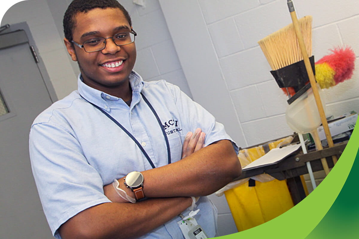 MCTI Custodial program student smiling with arms crossed with cleaning equipment in the background.