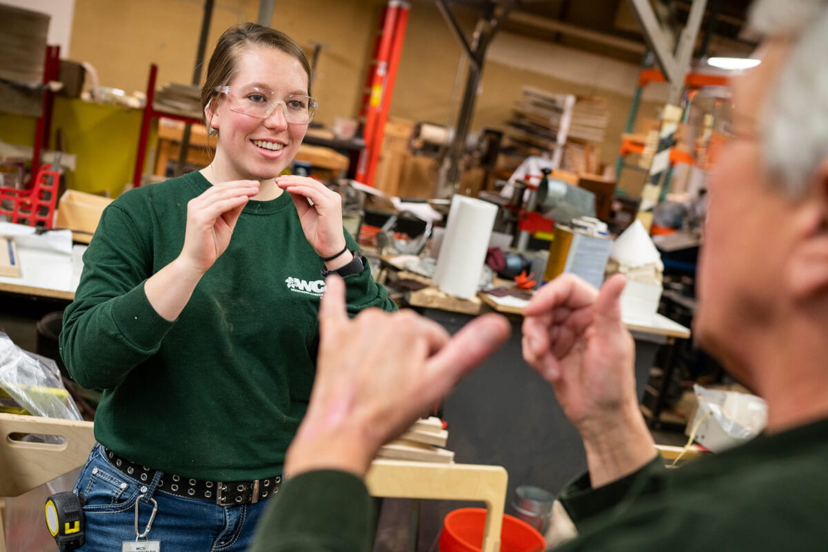 An MCTI student in the Cabinetmaking/Millwork Program using sign language to communicate with an instructor in a woodshop.