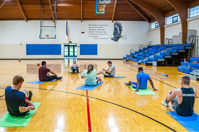 A group of MCTI students seated on yoga mats in a gymnasium during a fitness class.
