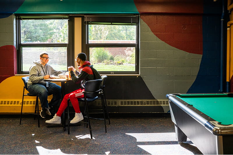 Two MCTI students sitting together at a high-top table in the indoor recreational area, known as The Canteen, on campus.