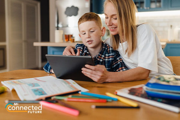 woman and school aged child looking at tablet at a table with school books and supplies