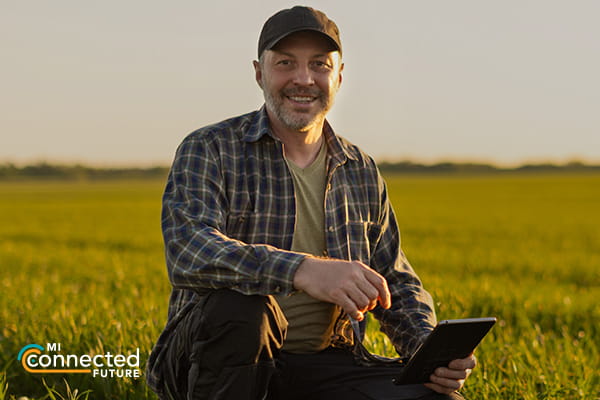 man sitting in a field with a tablet smiling at camera