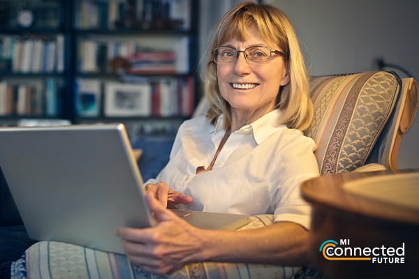 older lady sitting in an armchair holding a laptop smiling at the camera
