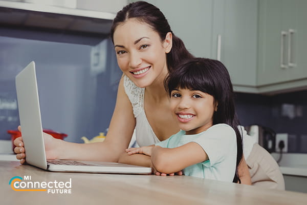 woman and school aged child sitting at a table with laptop smiling at camera