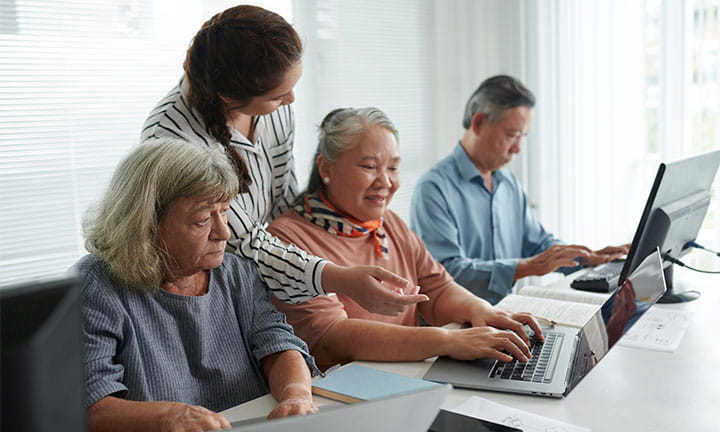 three senior citizens using computers while a woman gives them instruction